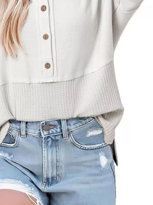White waffle-knit t-shirt with button detail and textured hem, paired with distressed denim shorts.