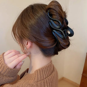 Black sculptural hair claw with serpentine design, acrylic and alloy, securing a bun.