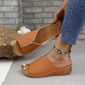 Asymmetrical vegan leather slides in caramel with white stitching and a peep toe.