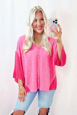 Hot pink V-neck blouse with contrast panels and raw hem detail.