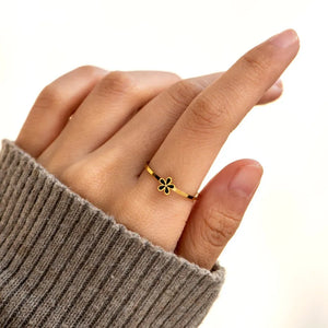 Delicate gold ring with black floral enamel detail on a hand wearing a grey sweater.