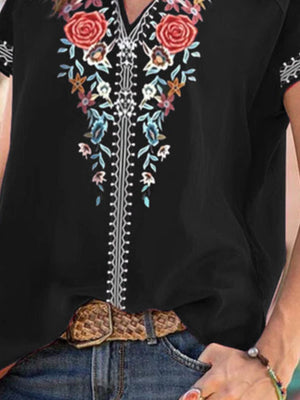 Black blouse with floral embroidery and notched neckline, styled with jeans and a belt.