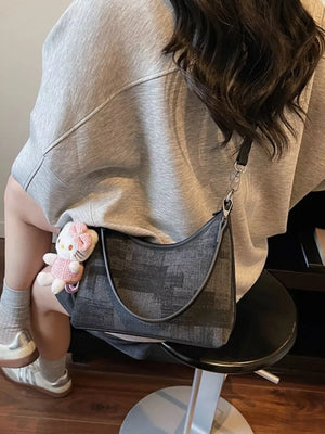 Crescent mini shoulder bag in black pu leather with textured pattern, worn with a Hello Kitty charm.