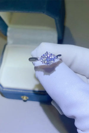 Silver moissanite trilogy engagement ring with a central round-cut stone and two smaller stones.