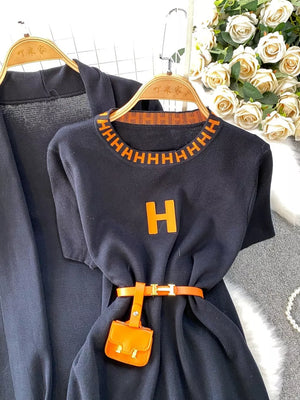 Black knitted maxi dress and cardigan ensemble with orange trim, H logo, and belt with charm.