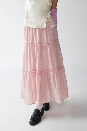Tiered cotton maxi skirt in blush pink with ruffled tiers, styled with a white lace-trimmed top.