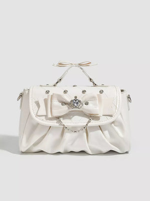 White ruched crossbody bag with bow, rhinestone crown, and chain detail