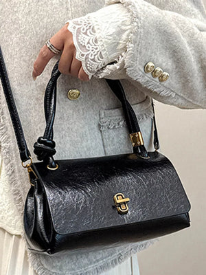 Black leather crossbody bag with twisted handle and gold clasp detail