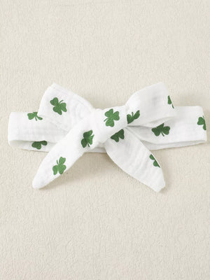 White cotton baby headband with green shamrock print and a bow detail.