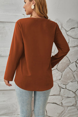 Rust v-neck button-down blouse with cuffed long sleeves and a curved hem.