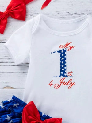 White baby onesie with "My 1st 4 July" patriotic graphic, red bow, and star bloomer.