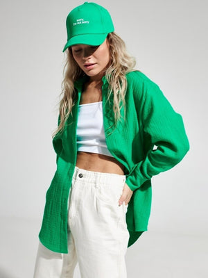Green textured cotton overshirt with relaxed fit and button front, styled with white tank top and cream pants.