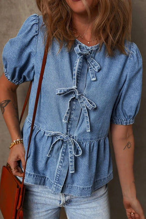Denim peplum blouse in medium wash with puff sleeves and multiple front bow ties.