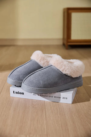Gray suede house slippers with plush shearling trim and decorative stitching.