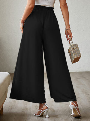 Black paperbag waist palazzo pants with side slits and textured fabric.