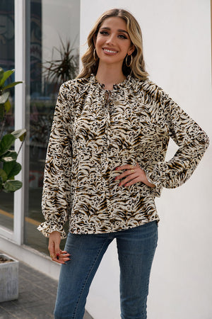 Animal print blouse with ruffle neckline and tie detail, long sleeves, and ruffled cuffs.