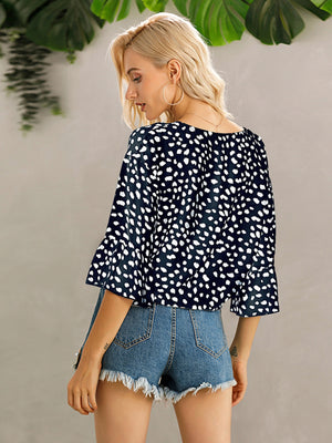 Dark blue spotted knot-front blouse with flared sleeves and a scoop neck.