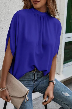 Royal blue blouse with draped sleeves and mock neck, styled with jeans.