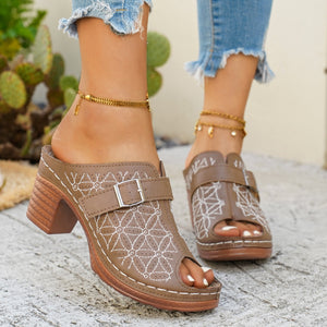 Tan buckle sandals with white floral embroidery and a block heel.