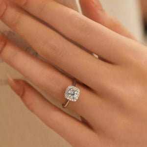 Elegant moissanite and sterling silver ring with a cushion-cut center stone surrounded by a halo of brilliant stones.