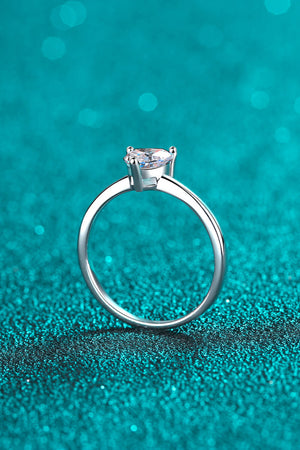 Silver heart-cut moissanite solitaire ring on a sparkly teal background.