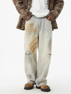Distressed light wash wide-leg jeans with unique tan paint splatters and ripped knee details.