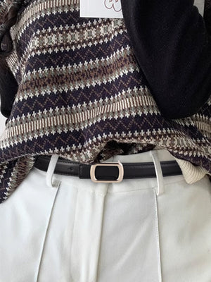 Black leather skinny belt with modern gold buckle, styled with white pants and a patterned sweater.