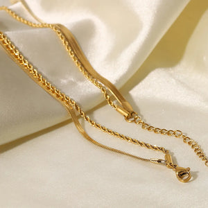 Gold serpentine and rope chain necklaces layered on satin fabric