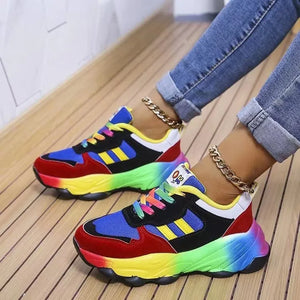 Rainbow gradient chunky sneakers with colorful laces and gold anklets.