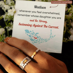 Adjustable rings with fish motifs, one gold, one silver, on a hand with a card.