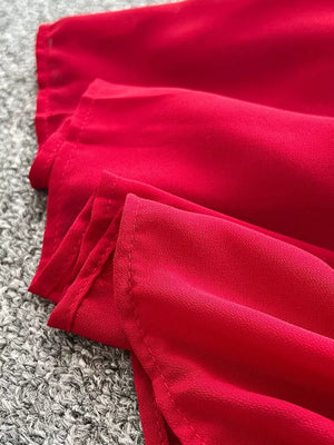 Red maternity maxi dress with one-shoulder neckline and floral accents, shown in a close-up of the fabric.