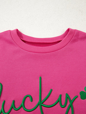 Pink crew neck sweatshirt with embroidered green lucky clover and script text detail.