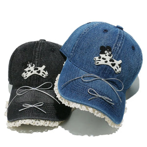 Denim baseball cap with puppy appliqué, lace trim, and bow details in light blue and black.