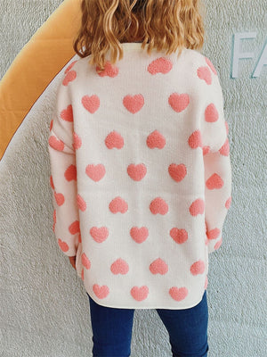 White acrylic cardigan with textured pink heart pattern, crew neck, long sleeves.