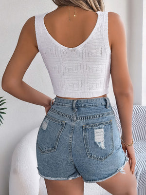 White knit crop top with a textured geometric pattern and V-neck, paired with distressed denim shorts.
