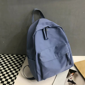 Dusty blue canvas school backpack with dual front pockets and zipper detail.