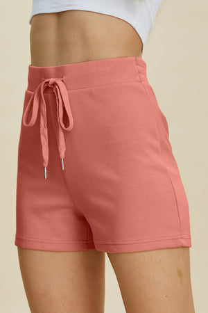 Coral drawstring sport shorts with a scuba fabric texture and elastic waistband.