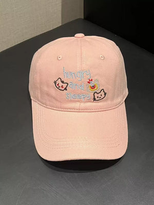 Light pink baseball cap with embroidered cats and text saying hungry and sleepy
