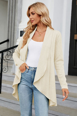 Cream cable knit drape-front cardigan with long sleeves, worn open over a white tank top and jeans.