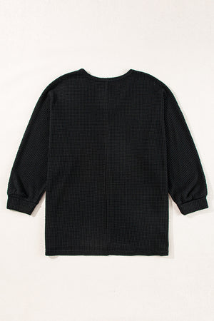 Black waffle knit V-neck top with long sleeves and a slit hem.