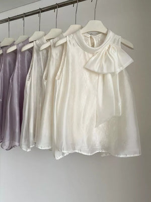 Sleeveless white shirt with a large bow detail and mock neck, available in purple and apricot.