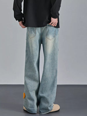 Men's light wash relaxed fit jeans with orange applique detail on the leg.