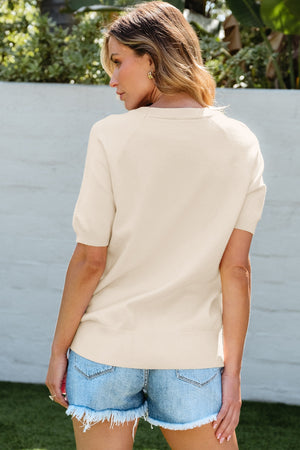 Ivory knit top with short sleeves and a ribbed hem, featuring a daisy appliqué detail.