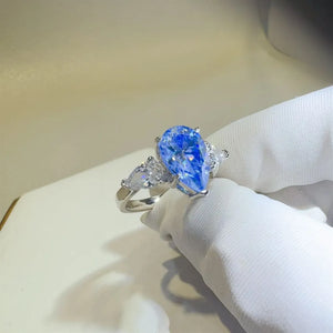Silver trilogy ring with a bright blue pear cut moissanite center stone and two pear cut side stones.
