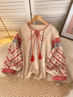 Apricot tie neck shirt with folk embroidery on sleeves and neckline, red tassels.