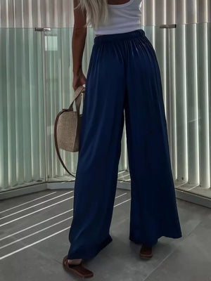 Dark blue maternity pants with paperbag waist and wide legs, styled with a white tank and straw bag.
