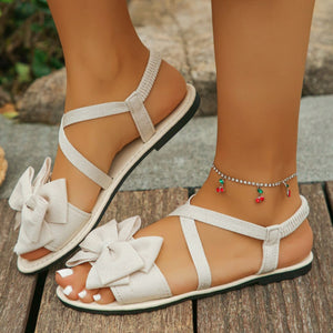 Off-white crisscross bow sandals with ankle straps and elastic heel band.