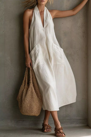 White halter midi dress with V-neck and large front pockets, styled with a straw bag.