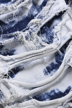 Distressed shredded denim jeans in medium wash with artistic blue tie-dye pattern and frayed edges.