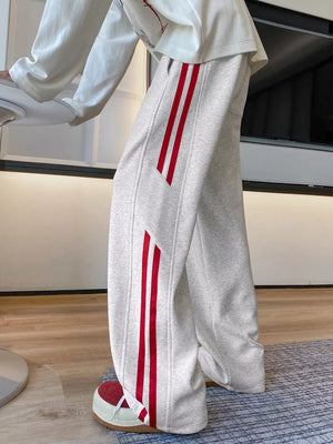 Men's light gray wide-leg sweatpants with bold red stripes on the sides.